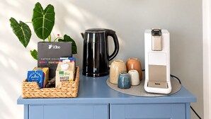 A kitchen counter with a coffee maker, a coffee pod dispenser, a basket of coffee pods, a coffee grinder, and a hanging plant.