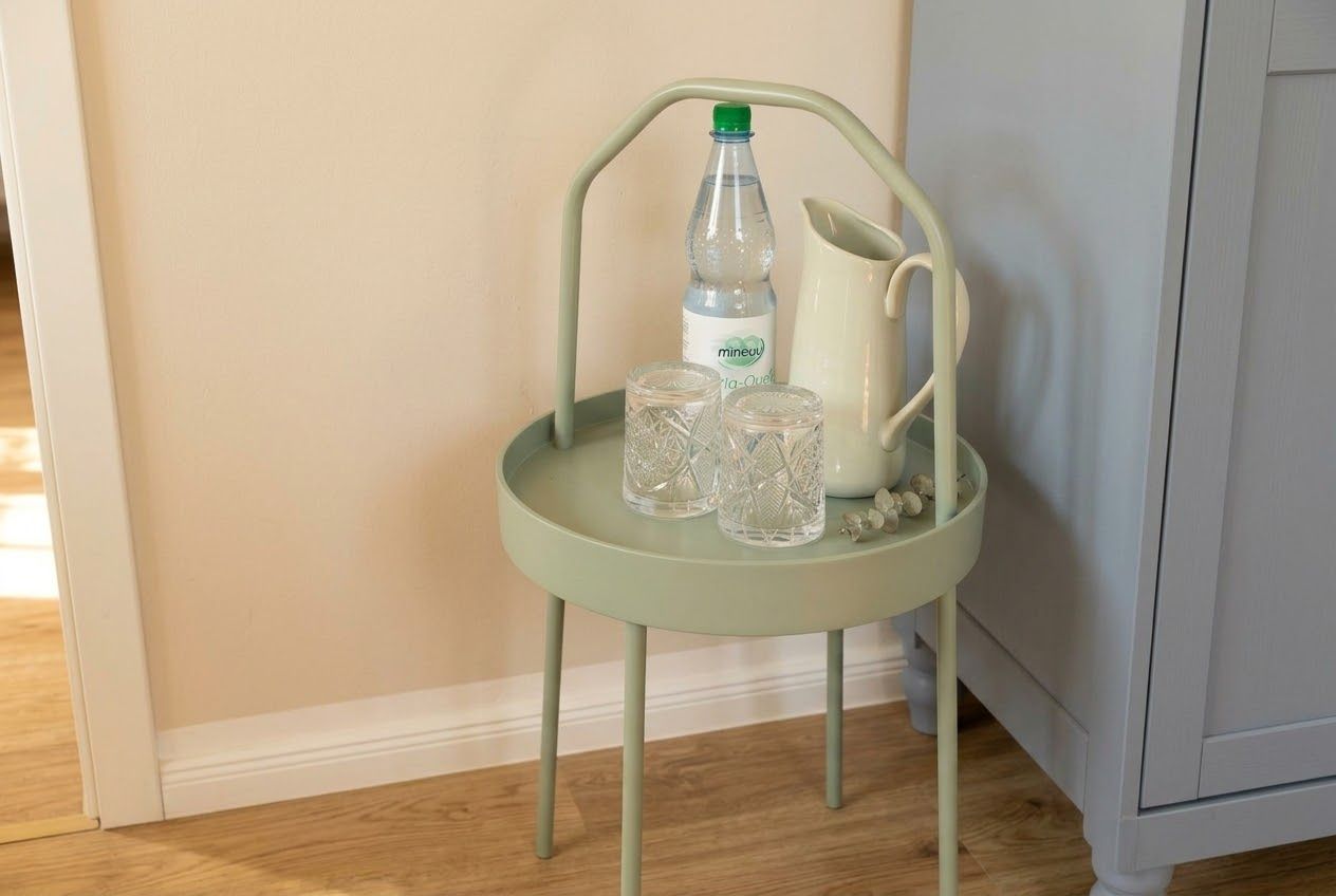 A light green metal chair with a white pitcher and two clear glasses on a tray.
