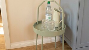 A light green metal chair with a white pitcher and two clear glasses on a tray.