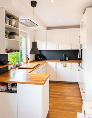 A modern kitchen with white cabinets, a wooden countertop, and a black pendant light.
