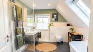 Un baño moderno con cabina de ducha de vidrio, bañera y ventana que proporciona luz natural.