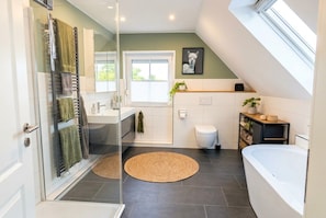 A modern bathroom with a glass shower enclosure, a bathtub, and a window providing natural light. - Vrbo Property (Ahlerstedt)