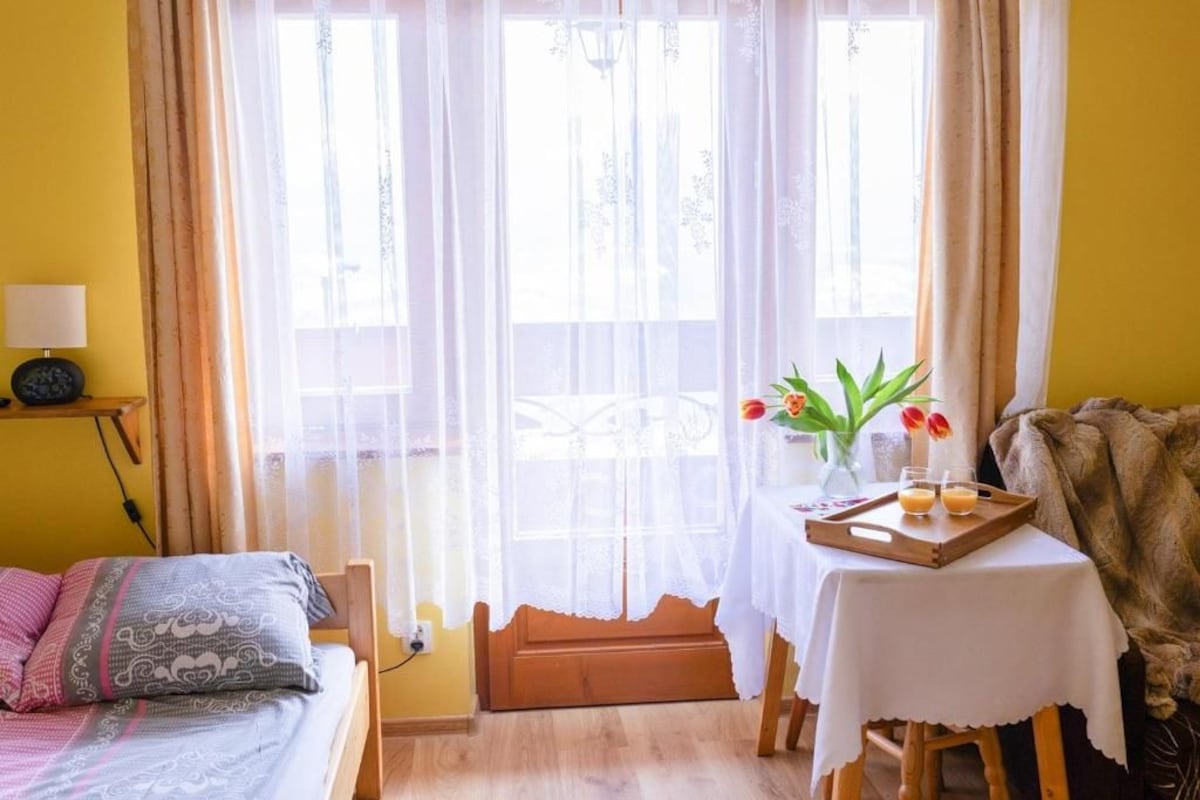 A room with a bed, a table with a tray of drinks, and a window with curtains.