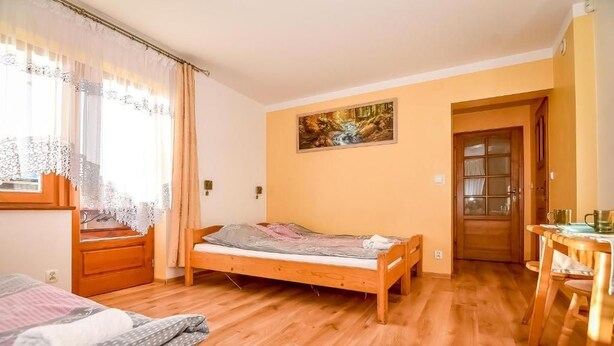 Un dormitorio con una cama de madera, una ventana con cortinas, un cuadro en la pared y una puerta de madera.