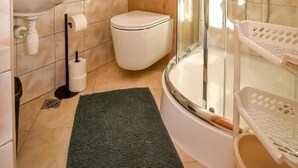 Un baño con cabina de ducha de vidrio, un lavabo, un inodoro y una alfombra verde.