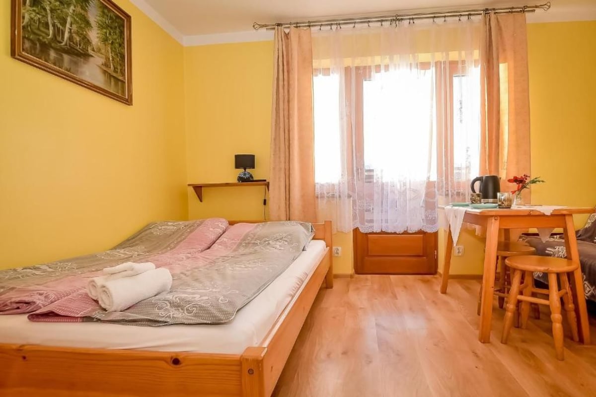 A room with a bed, a desk, a chair, a table, and a window with curtains.