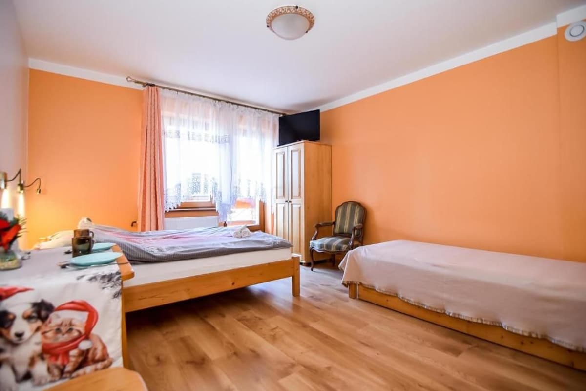 A room with a bed, a chair, a table with a lamp, and a window with curtains.