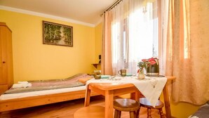 Una habitación con una cama, una mesa con taburetes, un ventanal con cortinas y un cuadro en la pared.