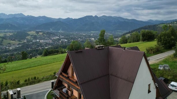 A residential building with a sloped roof, a view of a valley, and distant mountains. - Willa Piękne Widoki (Ząb)