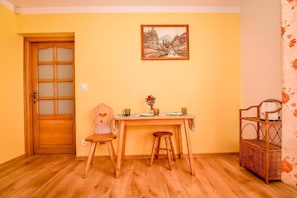 A room with a wooden door, a table with two stools, a wicker shelf, and a framed picture on the wall. - Willa Piękne Widoki (Poronin)