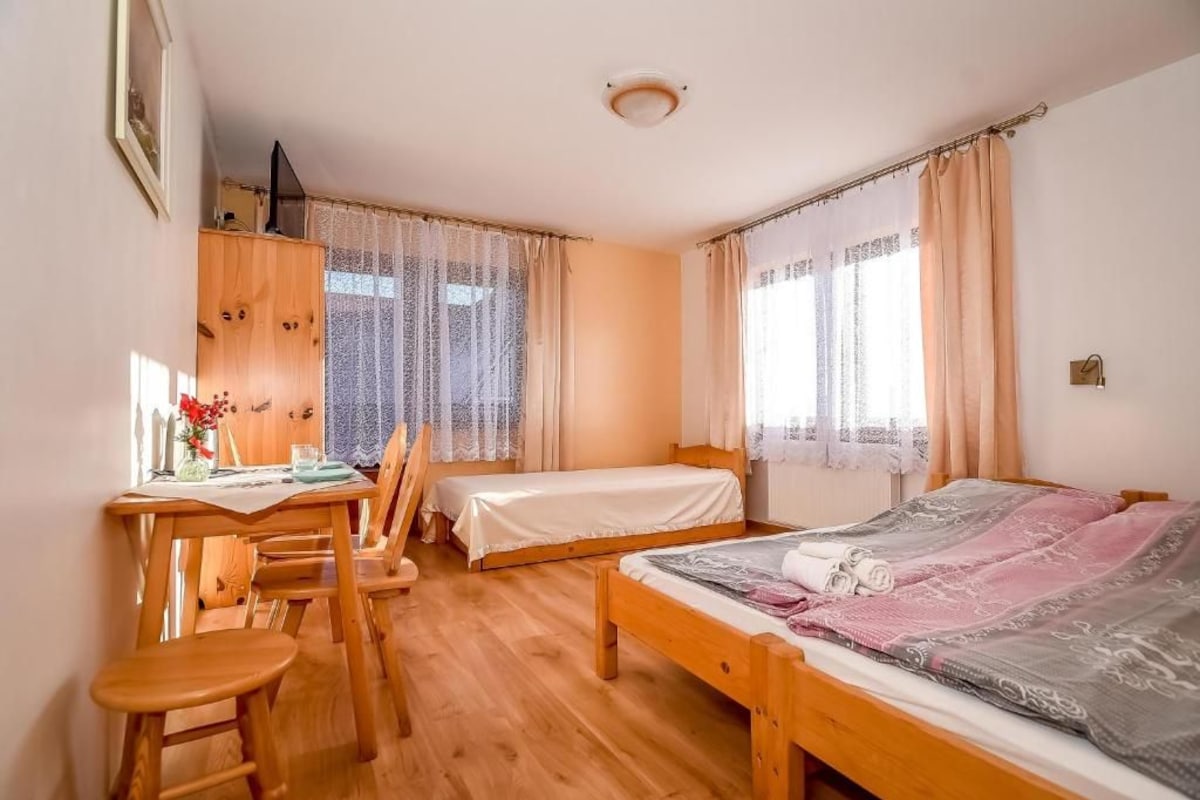 A room with two single beds, a wooden desk with a chair, and a window with sheer curtains.