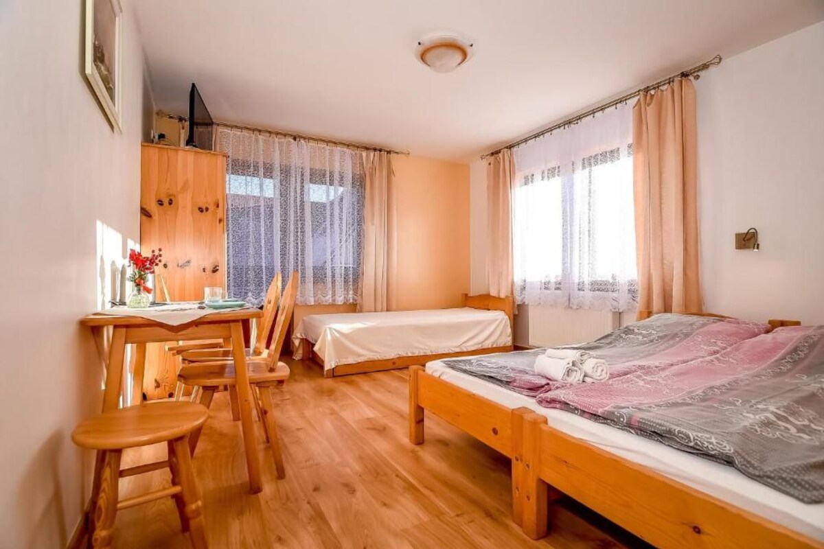A room with two single beds, a wooden desk with chairs, and a window with curtains.