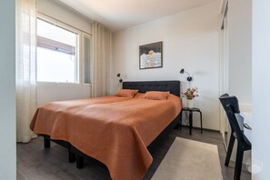A bedroom with a bed, a nightstand, a desk, a chair, a window with curtains, and a wall-mounted picture. - Polar Charm H Holiday in Lapland (Ylläs)