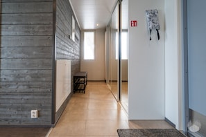 A hallway with a wooden wall, a bench, a fire exit sign, and a door with a patterned curtain. - Polar Charm H Holiday in Lapland (Ylläs)
