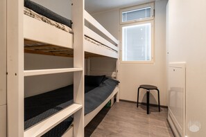 Ein Schlafsaalzimmer mit Etagenbetten, einem kleinen Hocker und einem Fenster mit Jalousien.