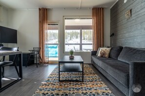 Een moderne woonkamer met een bank, een salontafel, een televisie en uitzicht op een besneeerd landschap door grote ramen.