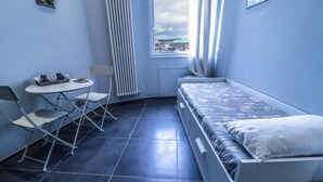 A small, compact room with a single bed, a table with chairs, and a window with curtains. - IL GRATTACIELO B&B (Napoli)