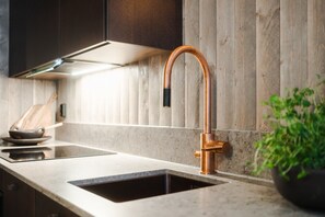 Une cuisine avec un robinet en cuivre, un évier et un pare-éclaboussures en bois.