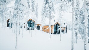 Lumipeitteinen maisema, jossa on puurakenteisia mökkejä ja niiden ympärillä puita.