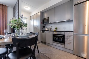 A modern kitchen with stainless steel appliances, a dining area with a table set for four, and a potted plant on the windowsill. - Polar Charm C by Holiday in Lapland (Ylläs)