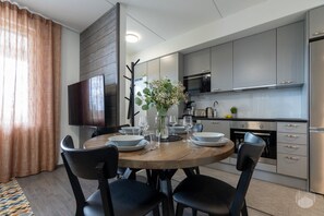 A modern kitchen with grey cabinets, a stainless steel refrigerator, and a dining area with a round wooden table and black chairs. - Polar Charm C by Holiday in Lapland (Ylläs)