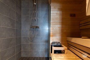 A sauna room with a wooden bench, a small table with stones, and a shower area with a hose. - Polar Charm C by Holiday in Lapland (Ylläs)