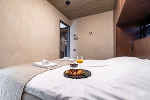 A hotel room with a bed, a tray of breakfast, a glass of orange juice, and towels.