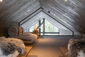 Quarto de sótão com teto inclinado, uma cama, uma mesinha de cabeceira e vista para o exterior.