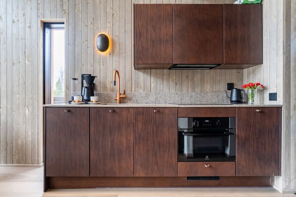 Une cuisine moderne avec des meubles en bois, un four encastré et une machine à café.