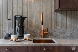 Une cuisine dotée d’un plan de travail en marbre, d’une machine à café, d’un mixeur, d’un robinet en cuivre et d’un mur en bois.