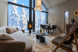 Um interior moderno com lareira, sala de jantar e vista para árvores cobertas de neve.