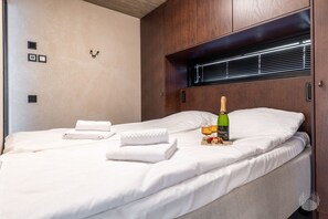 Uma cama bem arrumada com lençóis brancos, uma garrafa de champanhe e uma taça de vinho sobre a cama.