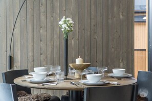 Une table de salle à manger ronde, avec de l’assiette blanche, des verres transparents et un chandelier comme décoration centrale.