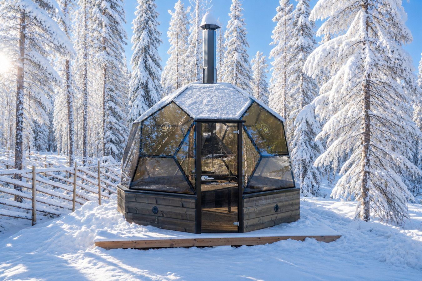 A hexagonal glass structure with a chimney, surrounded by snow-covered trees.