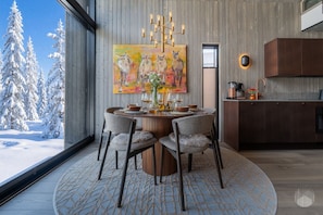 A modern dining area with a round table, chairs, and a painting above.