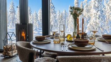 Un coin repas chaleureux avec une cheminée, des meubles en bois et une vue sur des arbres couverts de neige.