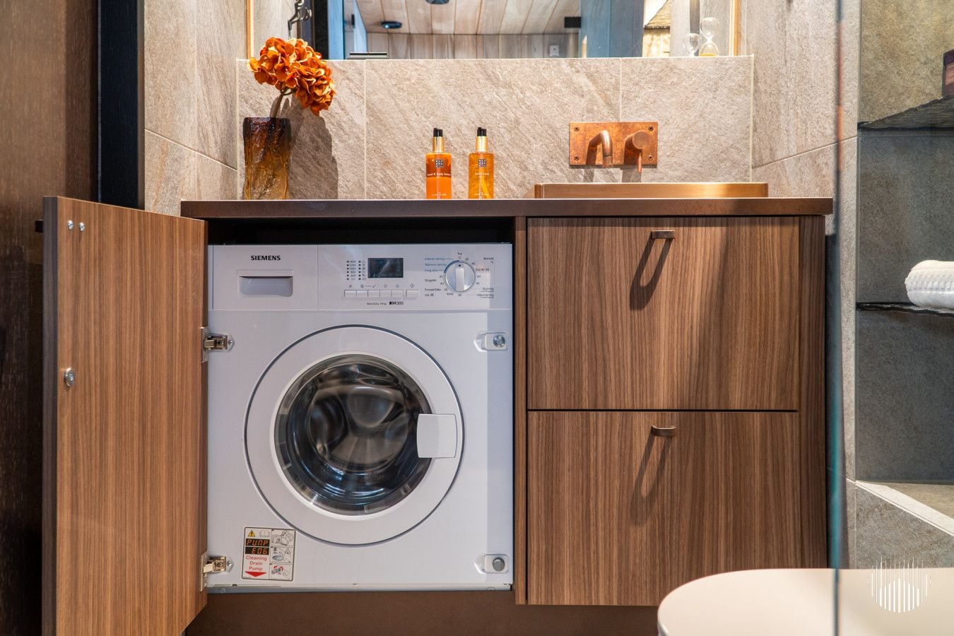 A modern bathroom with a built-in washing machine, wooden cabinetry, and a marble countertop.