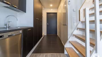 A modern kitchen with a dishwasher, a stainless steel sink, and a wooden staircase leading to a door.