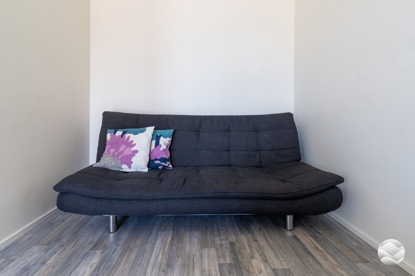 A dark-colored sofa with metal legs, two decorative pillows, and a wooden floor.