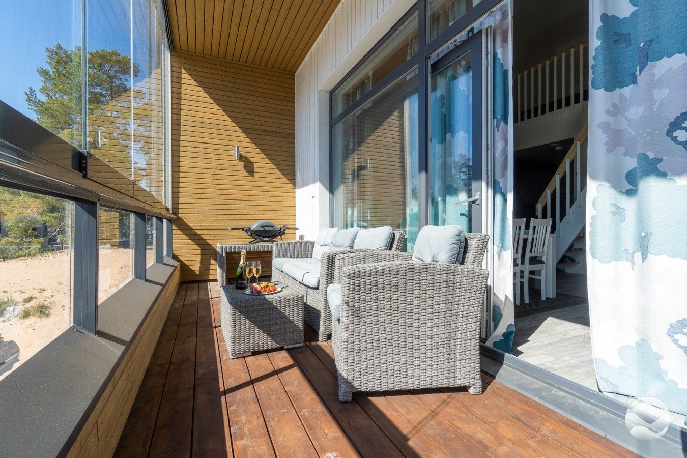 Ein Balkon mit Korbmöbeln, einem Grill und einem Esstisch mit Flasche und Gläsern.