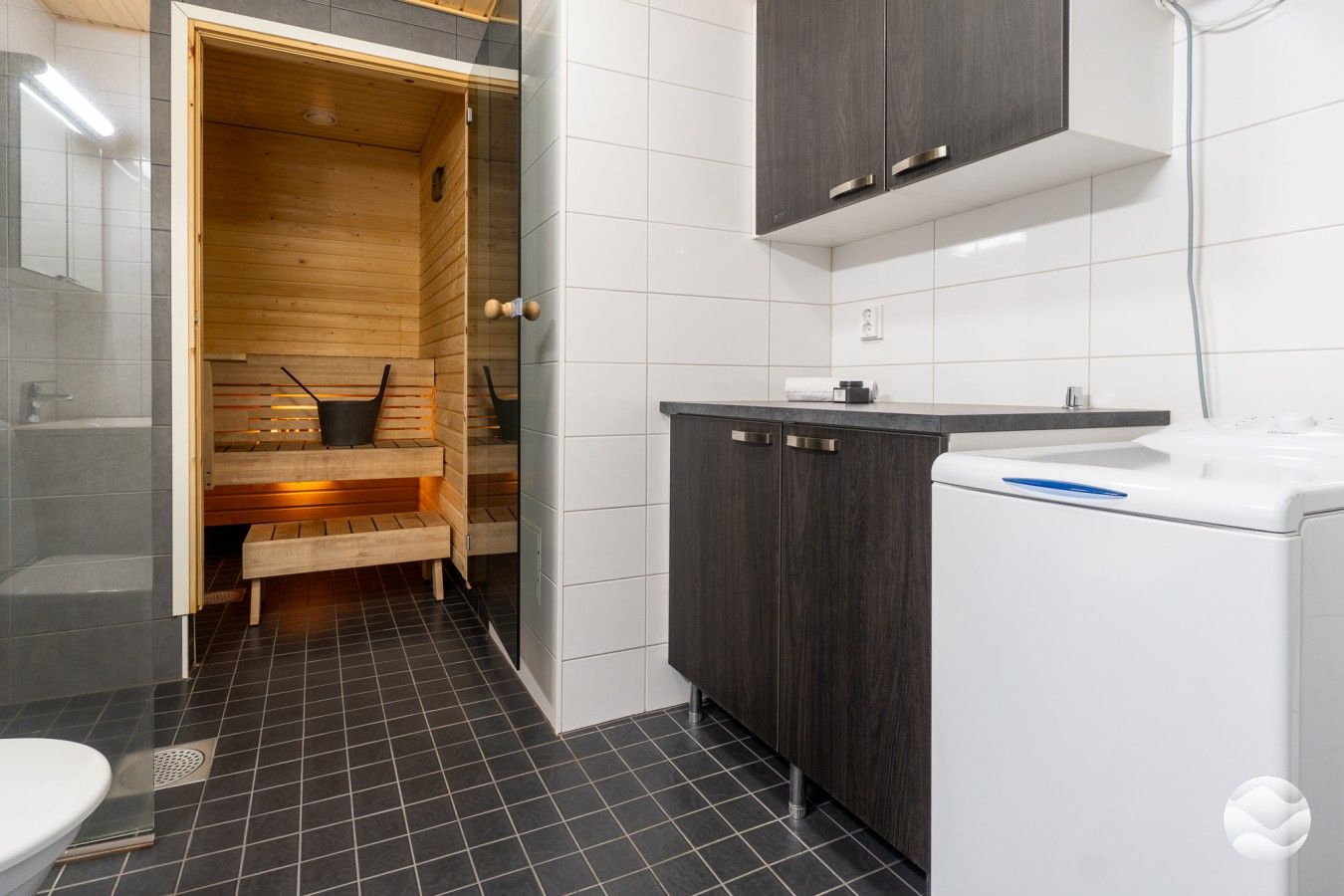 Un baño moderno con sauna, un lavabo blanco y armarios de madera oscura.