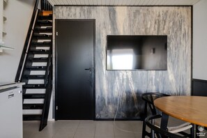 Eine moderne Küche mit schwarzer Tür, einer Treppe, einem an der Wand befestigten Flachbildfernseher und einem Esstisch mit Stühlen.
