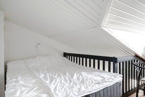 Ein Schlafzimmer mit Bett, schrägen Wänden und einem Fenster.
