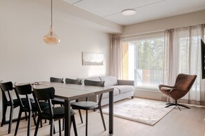 A modern dining area with a wooden table and chairs, a sofa, and a large window with curtains. - Äkäsentie 1 A 309 by Holiday in Lapland (Äkäslompolo)