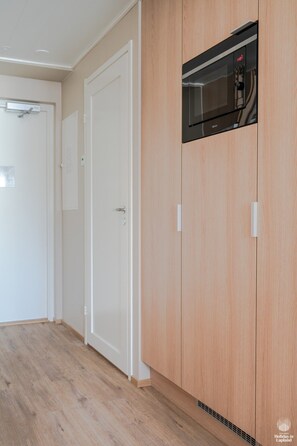 Ein Korridor mit Holzboden, einer weißen Tür und einem eingebauten Mikrowellenherd.
