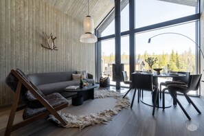 A modern living room with a large window, a sofa, a coffee table, and a dining area. - North Suite Sky by Holiday in Lapland (Levi)