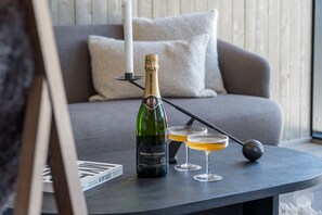 A bottle of Bernard-Massard Chardonnay, two glasses with a golden liquid, and a black object on a table in a room with a grey sofa and a white pillow. - North Suite Sky by Holiday in Lapland (Levi)