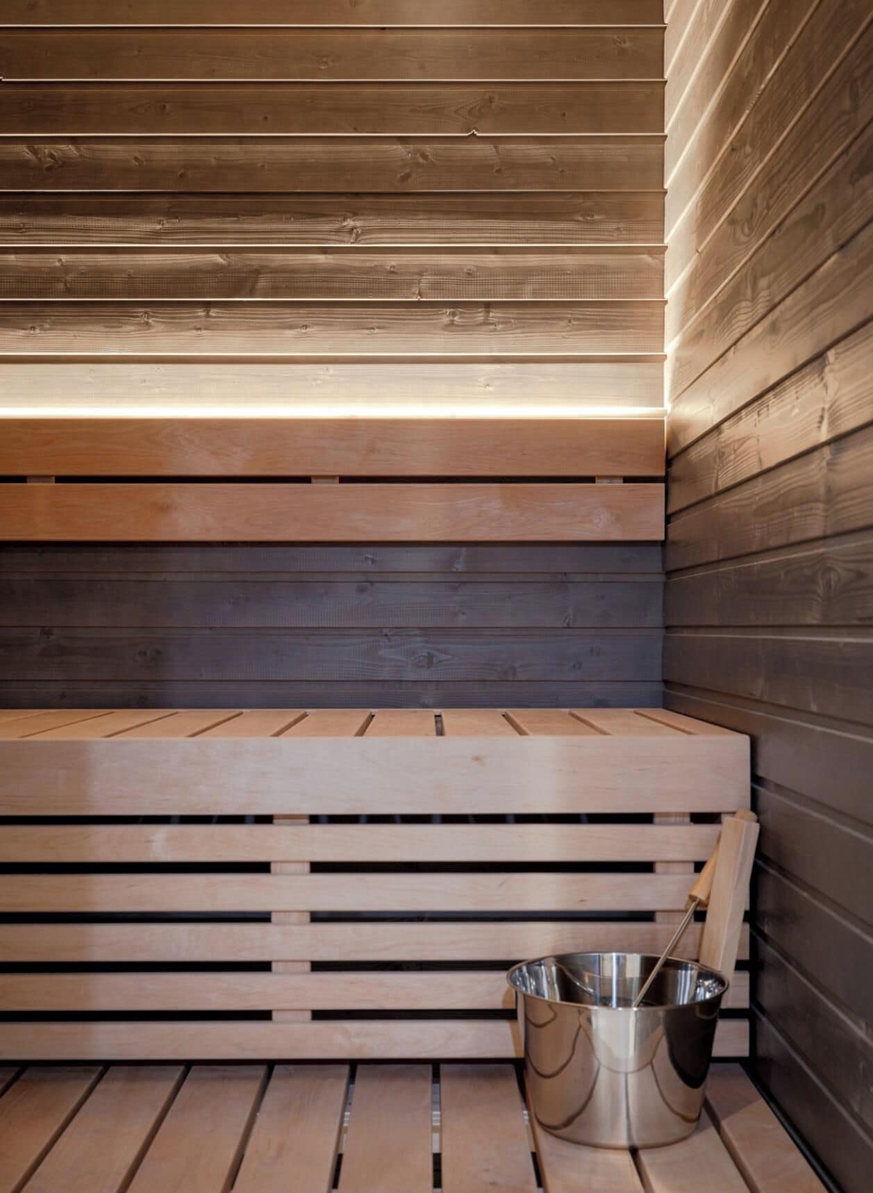 A sauna with wooden benches and a metal bucket.