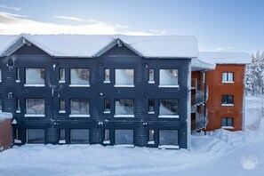 A multi-story building with a dark facade and snow-covered windows, featuring a red building adjacent to it. - Äkäsentie 1 A 202 by Holiday in Lapland (Äkäslompolo)