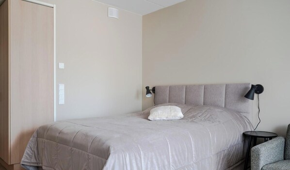 Een slaapkamer met een bed, nachtkastje, lamp en een deur.